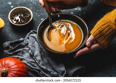 Woman In Yellow Knitted Sweater Eating A Pumpkin Cream Soup On Dark Stone Background With Spoon Decorated With Cut Fresh Pumpkin, Top View. Autumn Cozy Dinner Concept 
