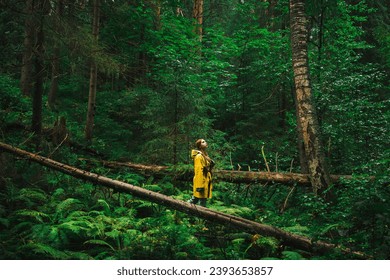 Woman in a yellow raincoat walk her way through a green wet forest during the rain. The concept of travel and tourism. - Powered by Shutterstock