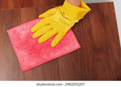 Woman in yellow rubber gloves cleaning wooden table with pink and yellow cloths - Powered by Shutterstock
