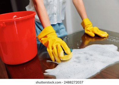 Woman in yellow rubber gloves cleaning table with soapy water and red bucket - Powered by Shutterstock