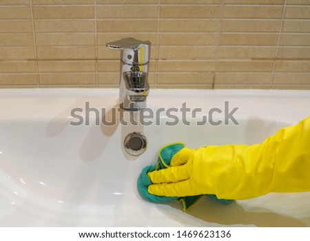 Woman in yellow rubber gloves cleaning a white water sink. Housewife holding a green rag. Modern bathroom. Cleaning company services. Housemaid washes the apartment.