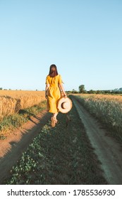 Woman In Yellow Sundress Walking By Wheat Field