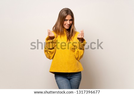 Woman with yellow sweater over isolated wall making money gesture