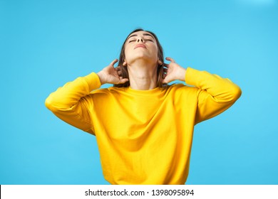 A woman in a yellow sweater tilted her head back against a blue background  