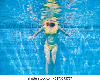 Woman In Yellow Swimming Suit In Clear Blue Water In Pool