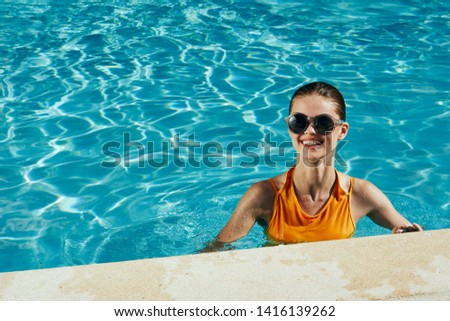 A woman in a yellow swimsuit and glasses transparent water pool                 