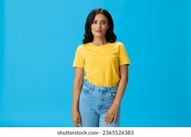 Woman in yellow t-shirt on blue background posing gestures emotions and signals with smile, hands up happiness copy space - Shutterstock ID 2365526383