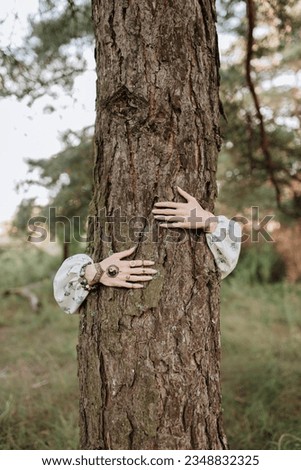 Woman with a yin yang sign on her hand and bracelets with magic hugs a big tree.