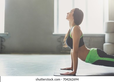 Woman in yoga class making upward-facing dog pose. Variation of svanasana for back startching. Healthy lifestyle in fitness club, copy space on wall