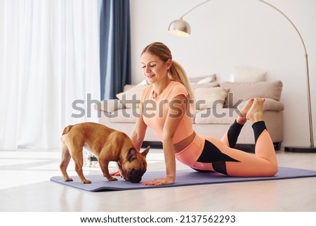 Woman in yoga clothes with pug dog is at home at daytime.