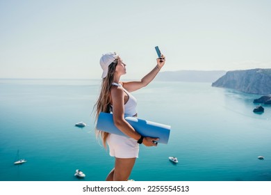 Woman with yoga mat over calm azure sea. Well looking middle aged woman with long hair, fitness instructor with blue yoga mat near the sea. Female fitness yoga routine concept. Healthy lifestyle. - Shutterstock ID 2255554513