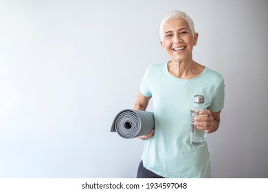 Woman with yoga mat while standing in fitness studio. Woman With Rolled Up Exercise Mat In Gym. Portrait of confident mature woman with exercise mat smiling in gym - Powered by Shutterstock