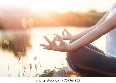 Woman yoga practicing and meditating by the lake in summer background