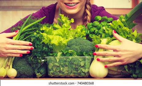 Woman Young Positive Housewife In Kitchen With Many Green Leafy Vegetables, Fresh Produce Organically Grown On Counter. Healthy Lifestyle, Cooking, Vegetarian Food, Dieting And People Concept.