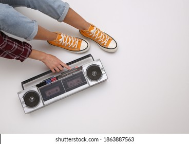 Woman In Youth Clothing Retro 80s Style Turns On Audio Boombox Tape Recorder While Sitting On White Background