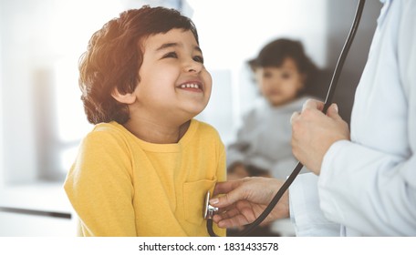 Woman-doctor examining a child patient by stethoscope in sunny clinik. Cute arab boy at physician appointment