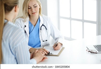 Woman-doctor and patient sitting and talking in hospital or clinic. Blonde therapist is cheerfully smiling. Medicine concept - Shutterstock ID 1845205804