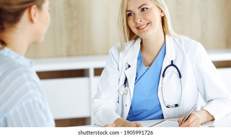 Woman-doctor And Patient Sitting And Talking In Hospital Or Clinic. Blonde Therapist Is Cheerfully Smiling. Medicine Concept