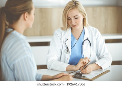 Woman-doctor And Patient Sitting And Talking In Hospital Or Clinic. Blonde Therapist Is Cheerfully Smiling. Medicine Concept