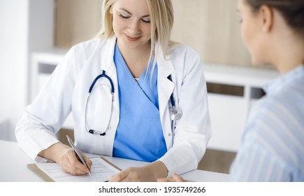 Woman-doctor and patient sitting and talking in hospital or clinic. Blonde therapist is cheerfully smiling. Medicine concept
