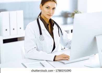 Woman-doctor typing on pc computer while sitting at the desk in hospital office. Physician at work