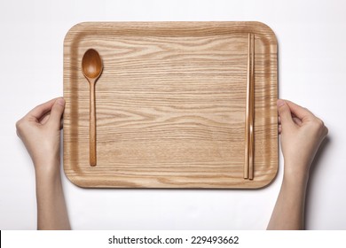 A woman(female) two hands hold a empty(blank) wooden tray with wooden spoon and chopsticks isolated white, top view, studio.