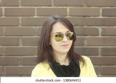 The womanly adult girl in sunglasses against the background of a brown brick wall - Shutterstock ID 1380696911
