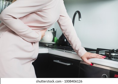 Woman's Abdominal Pain. The Woman In The Kitchen Is Holding Her Belly, She Feels A Strong Stomach Ache. Indigestion, Stomach Problems. Medical Concept.