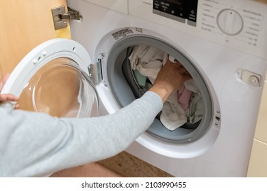 Woman's arm filling the washing machine drum. Concept of energy consumption, high price of electricity, household chores, housewives, turning on the washing machine. - Shutterstock ID 2103990455