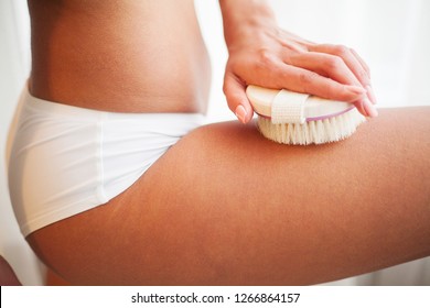 Woman's arm holding dry brush to top of her leg. Cellulite treatment, dry brushing.