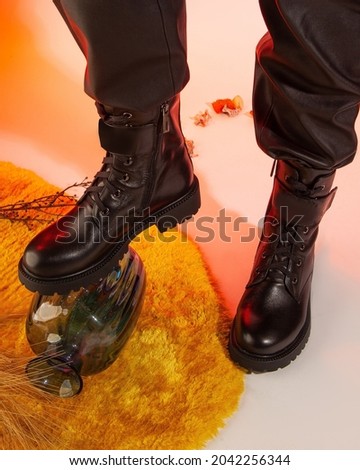Woman's autumn black leather boots with legs on color background studio shot.