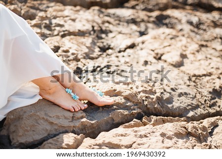 Woman's bare feet with elegant pedicure and bracelets on the rocks, close-up. Woman sitting on the rocky beach