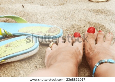 Woman's bare feet and red painted toenails in the sand. Sandy beach. Flip flops. Ankle bracelet. Female. Feminine. Relaxation. Leisure. Vacation. Holiday. Barefoot. Toe ring. Close up. Hazy. Dreamy. 
