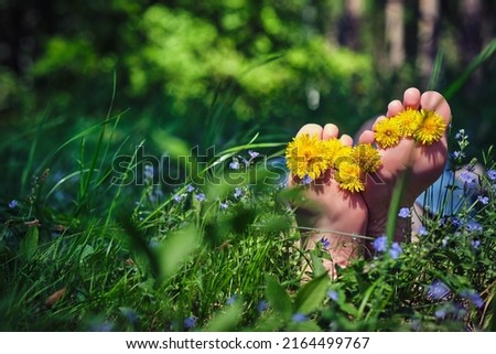 Woman's bare feet with yellow flowers between toes relaxing on green grass in sunny day. Freedom and healthy lifestyle. Summer vacation concept.