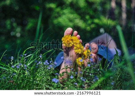 Woman's bare feet with yellow flowers between toes relaxing on green grass in sunny day. Freedom and healthy lifestyle. Summer vacation concept.