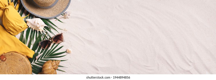 Woman's beach accessories: swimsuit, bikini, rattan bag, straw hat, shells, sunglasses, palm leaves on sand background. Exotic, tropical mood. Summer vacation, travel concept. Flat lay. Copy space.