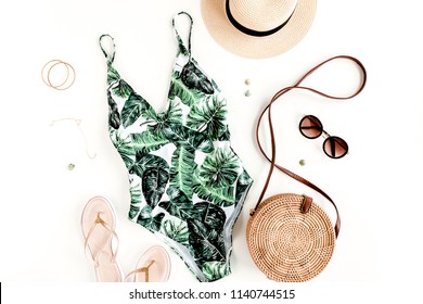 Woman's beach accessories: swimsuit with tropical print, rattan bag, straw hat on white background. Summer background. Flat lay, top view.