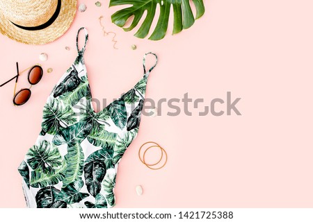Woman's beach accessories: swimsuit with tropical print, straw hat on pink background. Summer background. Flat lay, top view.