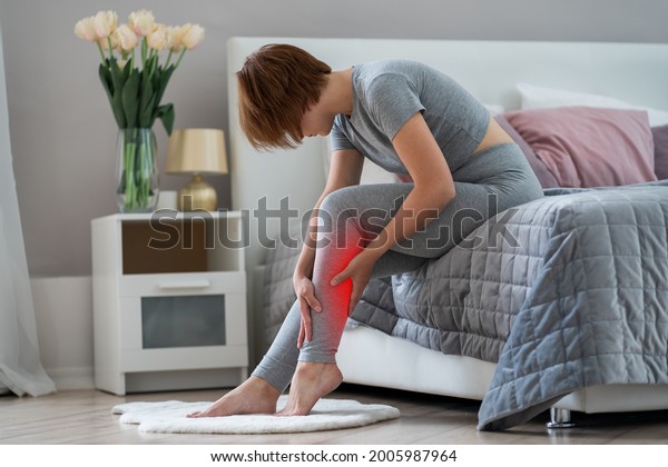 The woman\'s\
calf muscle cramped, massage of female leg in home interior,\
painful area highlighted in\
red
