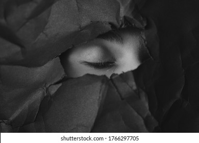 Woman's closed eye in hole in black crumpled paper background, black and white concept photography for blog or poster