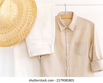 Woman's Cotton Elegant Outfit In Shades Of Beige With Straw Hat. Rack With Summer Female Clothes On Hangers Next To Wall. Clothing Retails Concept. Advertise, Sale, Fashion. Simplicity Concept.