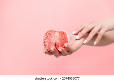 Woman's elegant hands hold half a grapefruit. Oil is poured on top of the fruit. Copy space. The concept of sexuality.