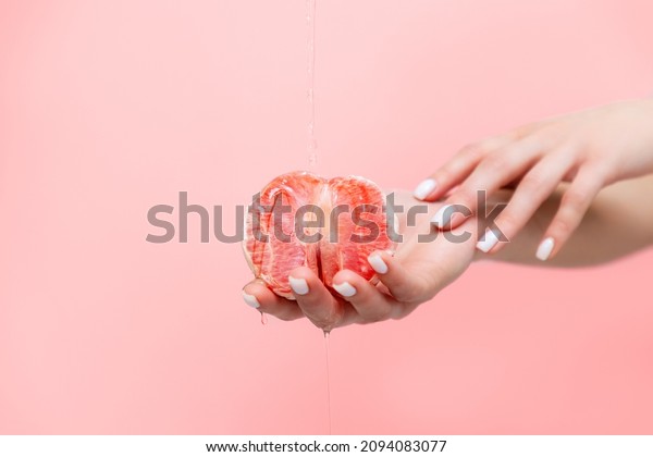 Woman\'s\
elegant hands hold half a grapefruit. Oil is poured on top of the\
fruit. Copy space. The concept of\
sexuality.