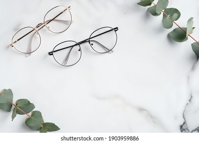 Woman's eyeglasses and eucalyptus branches on marble background. Flat lay, top view.