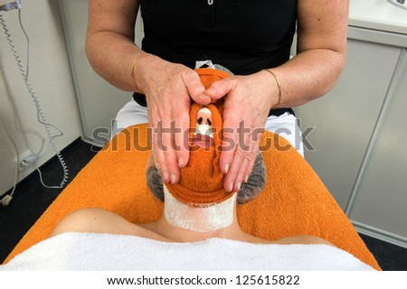 A woman's face is cleaned with a hot towel in a beauty salon