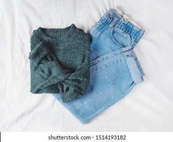 Woman's Fall Outfit With Green Sweater And Vintage Mom Jeans Isolated On White Linen Background. Flat Lay. Top View. Copy Space