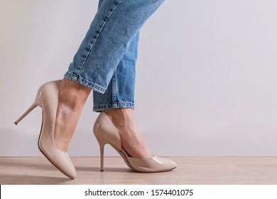 Woman's Feet Close-up Wearing High Heel Shoes And Jeans Standing On The Floor.