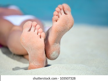 Woman's feet on the white sand near the sea.
