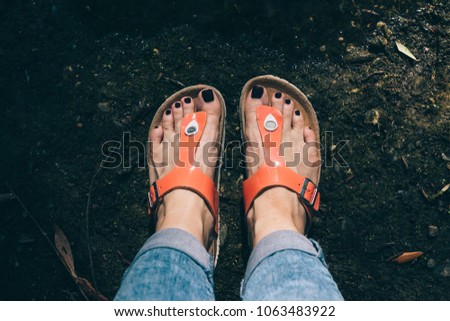 Woman's feet in orange sandals and jeans standing near the lake