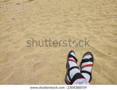 Woman's feet in socks and hiking sandals on hot beach sand during the day, copy space